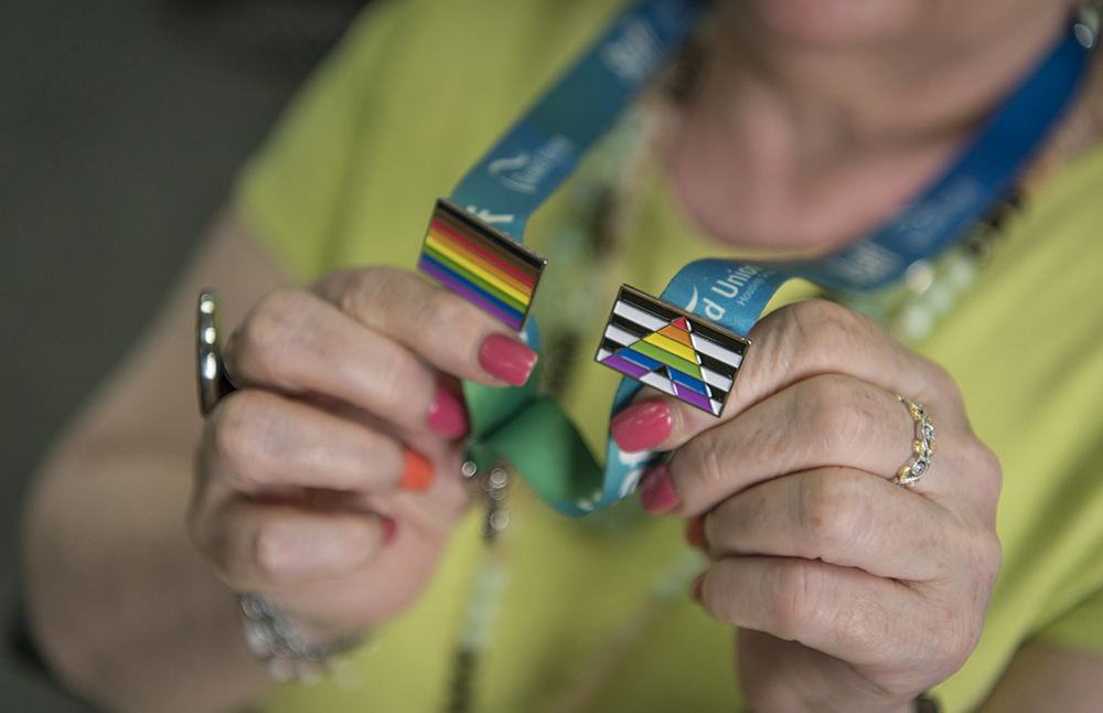 A colleague holding up their Pride and straight ally pin badges