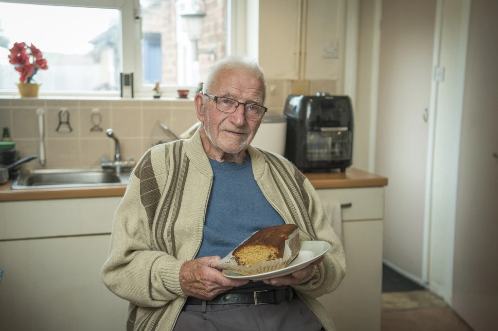 Dennis sitting in his kitchen holding his home made cake